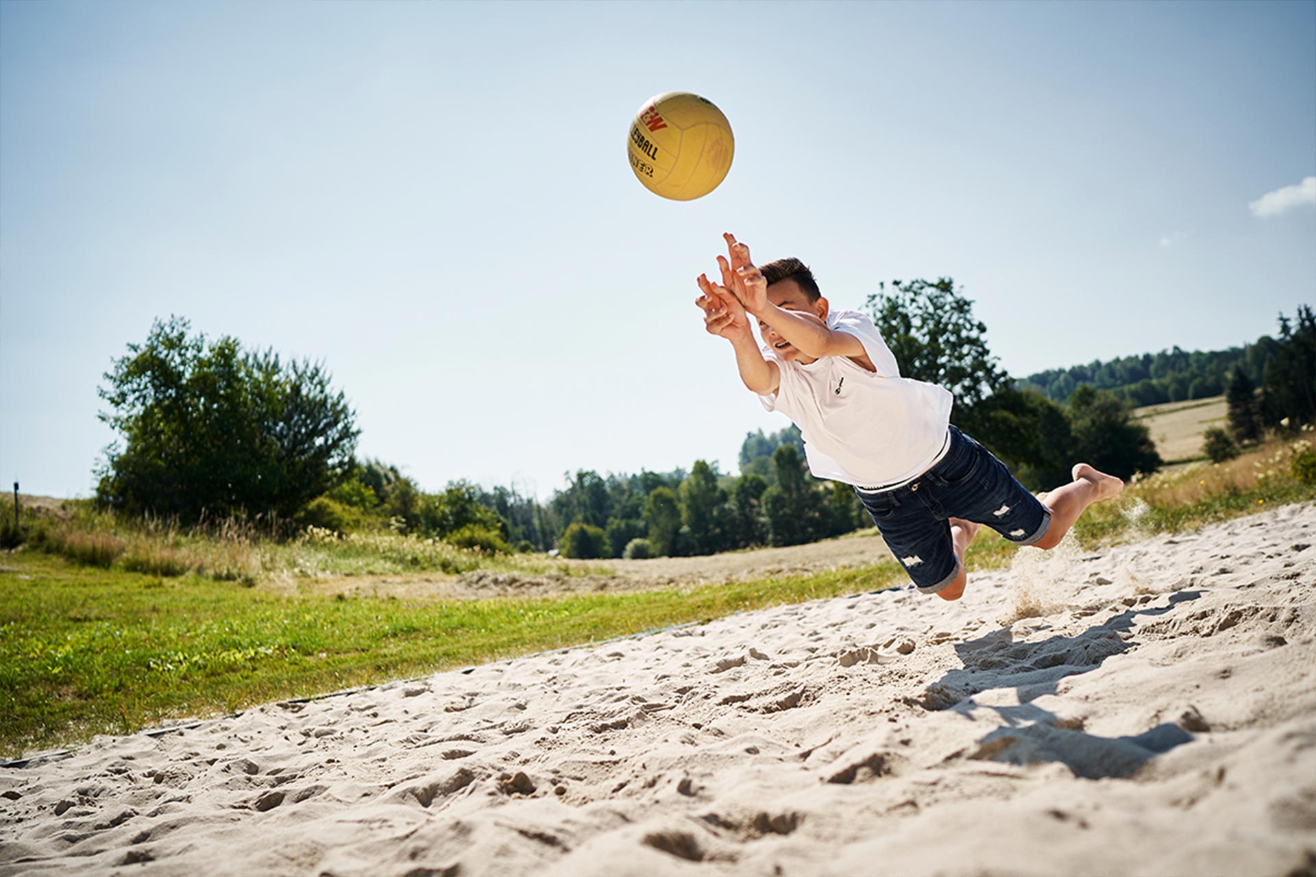 Junge macht einen Hechtsprung beim Beachvolleyball